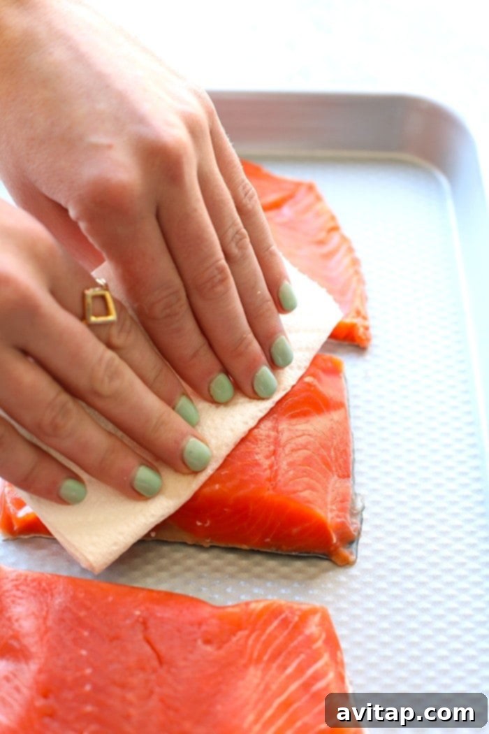 Hands gently patting salmon fillets dry with a paper towel, a crucial step for crispy skin.