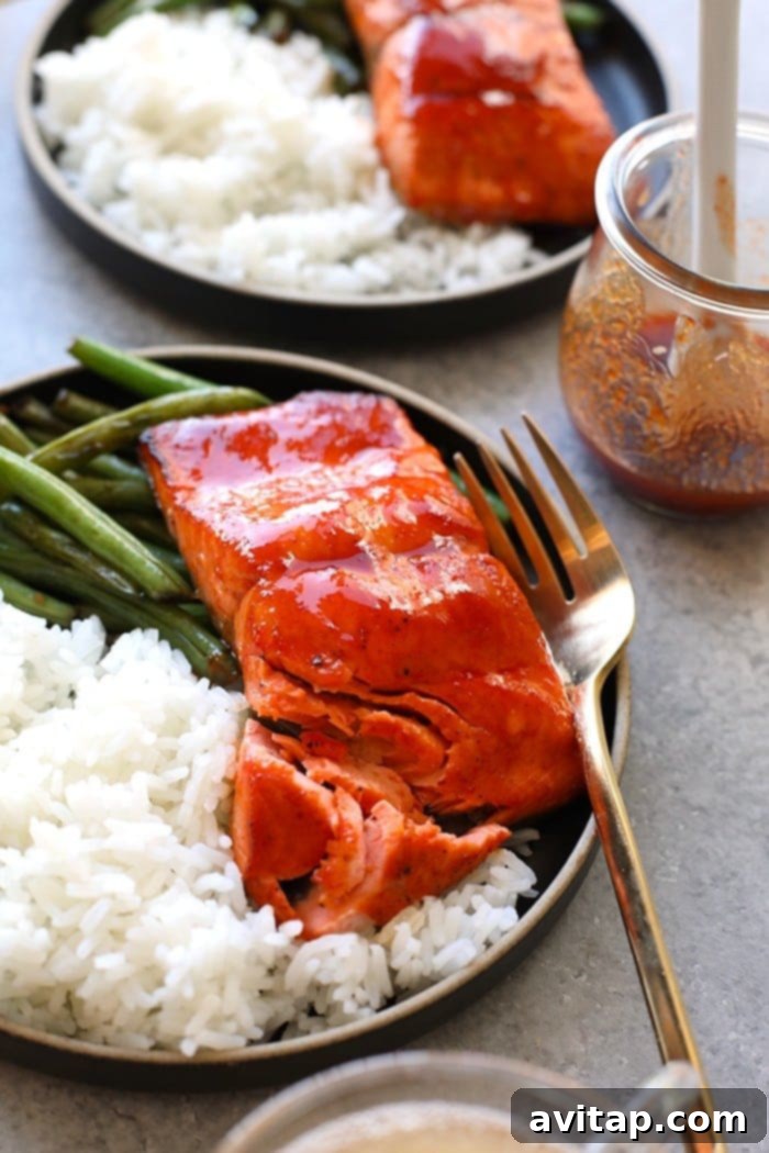 Whip up this amazing Honey Sriracha Salmon in just 8 minutes. All you need are 4 ingredients, and your oven broiler to make this protein-packed dinner that everyone will love! Perfectly cooked Honey Sriracha Salmon served on a plate with white rice and green beans.