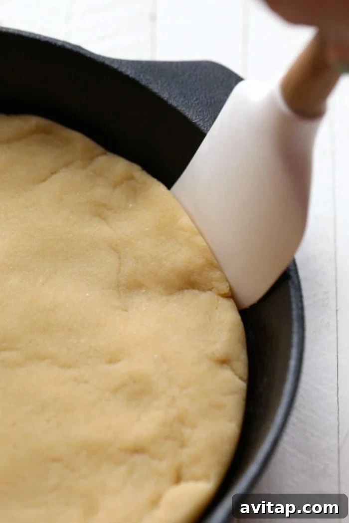 Hands pressing gluten-free sugar cookie dough into a round pan to form the crust of the fruit pizza.