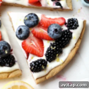 A complete healthy fruit pizza on a marble counter, garnished with fresh berries.