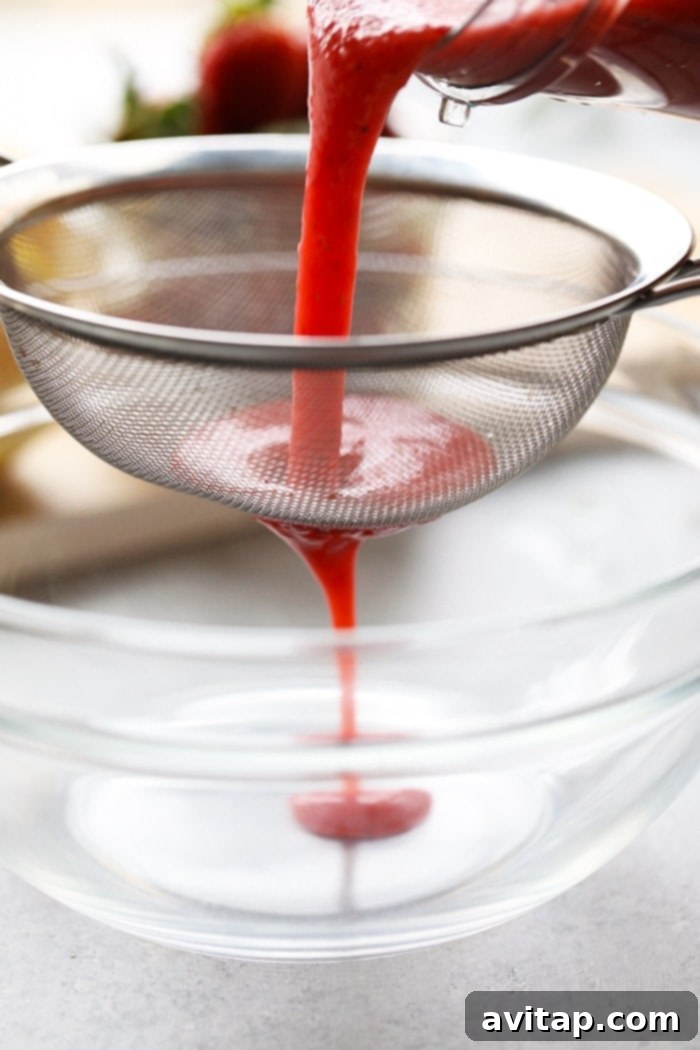 Strawberry puree being carefully strained through a fine-mesh sieve to remove seeds, ensuring a smooth and silky texture for the lemonade.