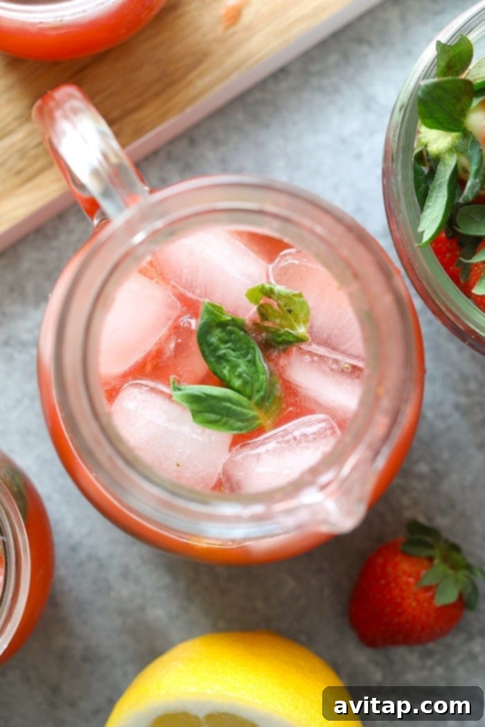 A large pitcher of homemade strawberry basil lemonade, garnished with lemon and strawberry slices, ready to be served.