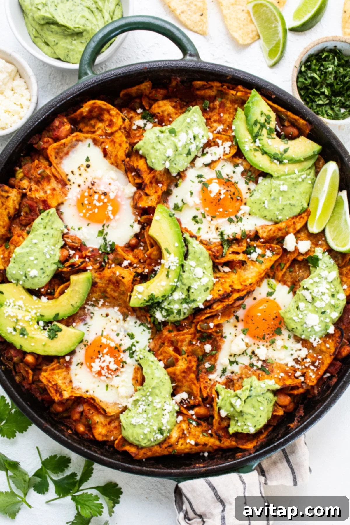 Easy Chilaquiles Recipe: Tomato Sauce, Spices, Beans, Tortilla Chips, Baked Eggs Delicious chilaquiles with creamy avocado crema served in a cast iron skillet.