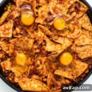 Eggs cracked over chilaquiles mixture in a skillet.