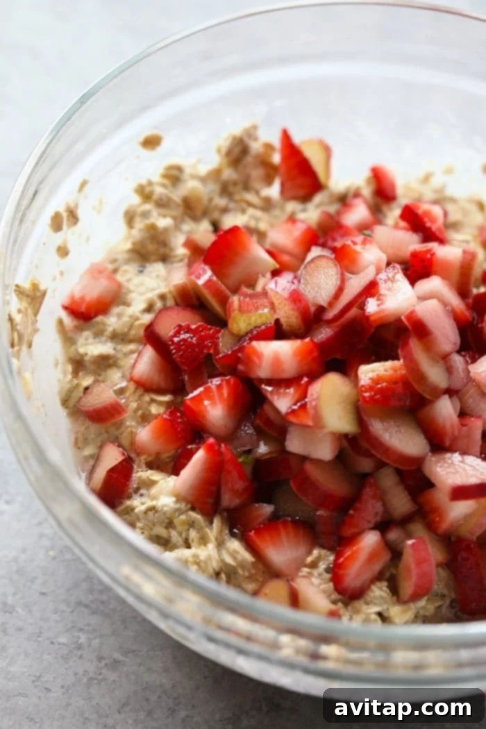 A bowl filled with freshly sliced strawberries and chopped rhubarb, ready to be combined with the oatmeal mixture for baking.