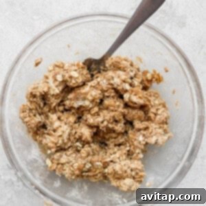 Peach crisp topping sprinkled on oats served in a bowl with a spoon.