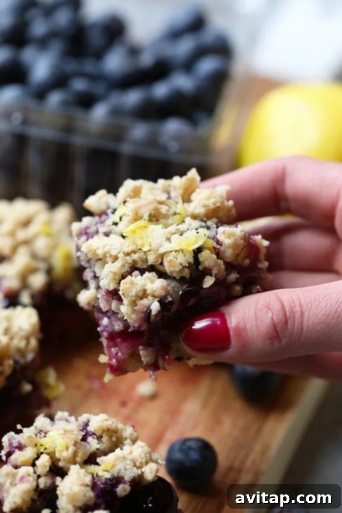 A hand holding a single delicious Lemon Blueberry Crumble Bar, showcasing its layers.