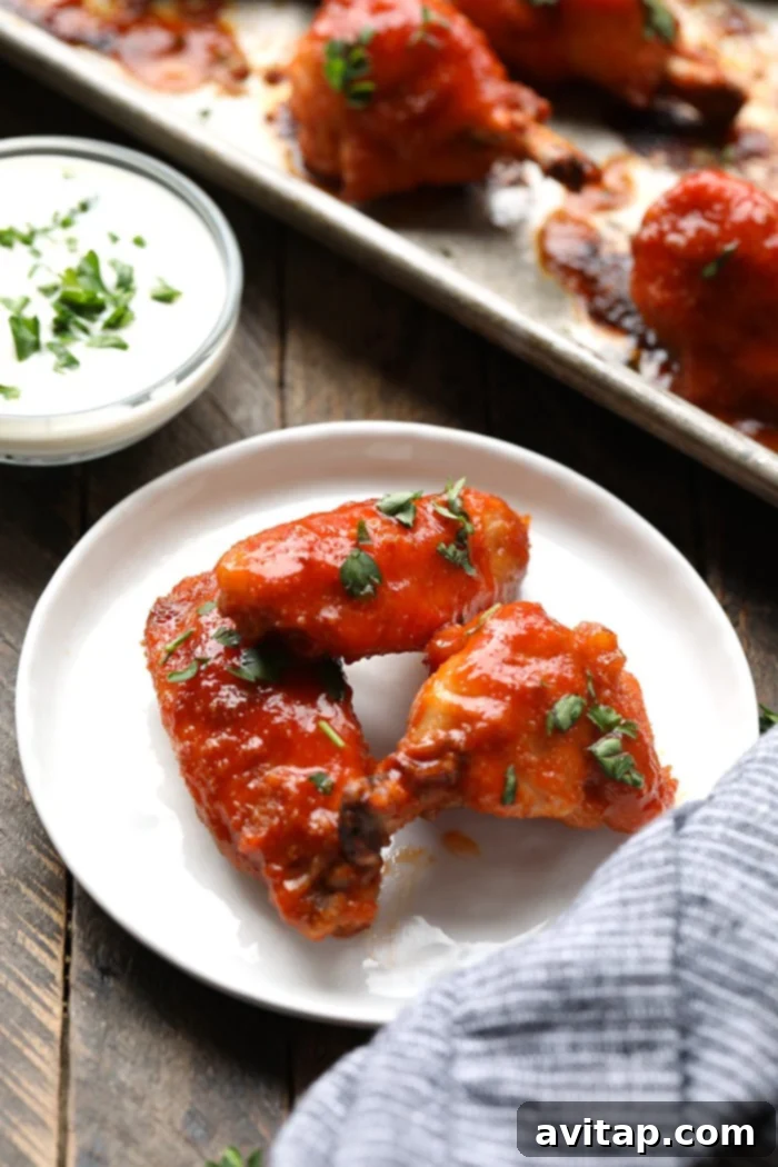 3 perfectly baked buffalo chicken wings on a clean white plate, garnished with fresh herbs.