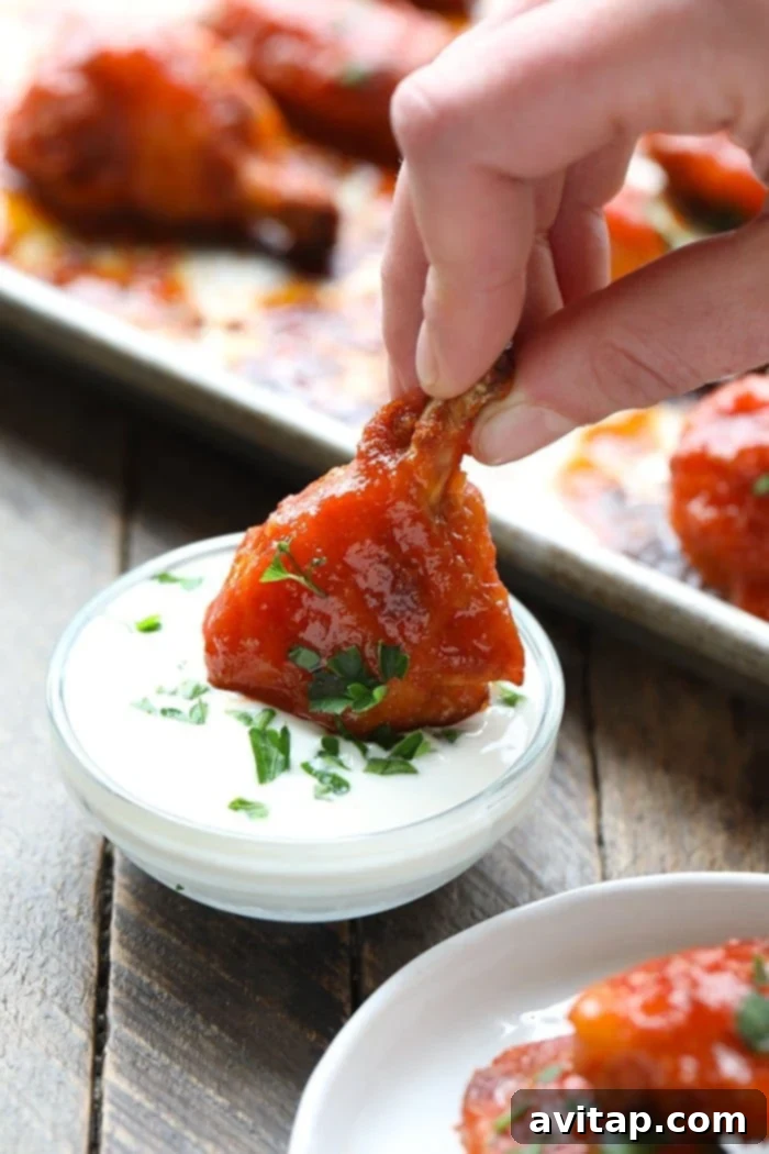 A perfectly baked buffalo chicken wing being dipped into a creamy, cool yogurt sauce, showcasing its crispy texture.