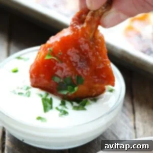A person enjoying baked chicken wings by dipping them into a bowl of sauce.