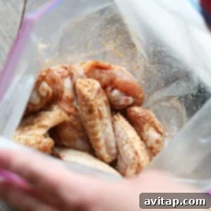 A person is placing chicken wings coated in dry rub into a plastic bag.