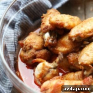 Baked chicken wings served in a bowl on a wooden table, freshly tossed in buffalo sauce.