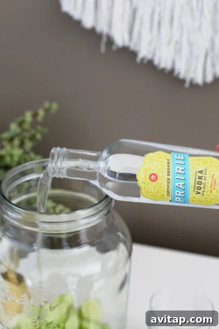 Pouring Prairie Organic Cucumber Vodka into a glass dispenser filled with fresh cucumber and honeydew melon slices.