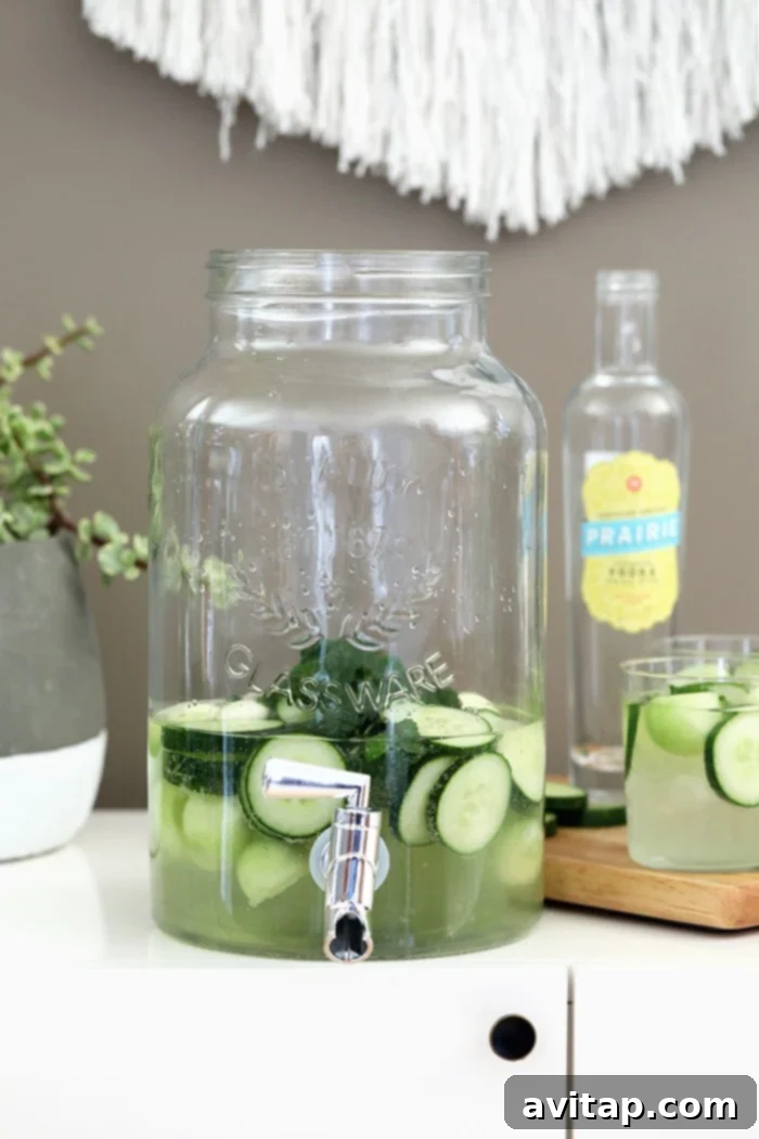 A large mason jar drink dispenser filled with the refreshing cucumber vodka cocktail, ready for a party.