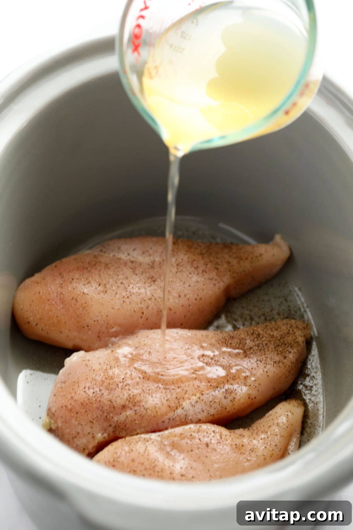 Raw chicken breasts nestled in a slow cooker with chicken broth, ready for cooking.