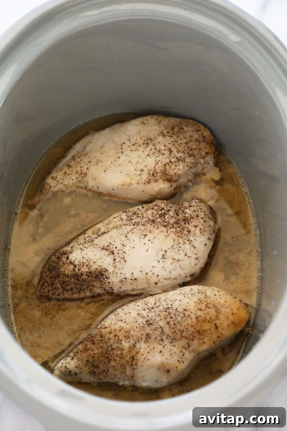 Cooked, whole chicken breasts resting in a slow cooker, surrounded by savory broth before shredding.