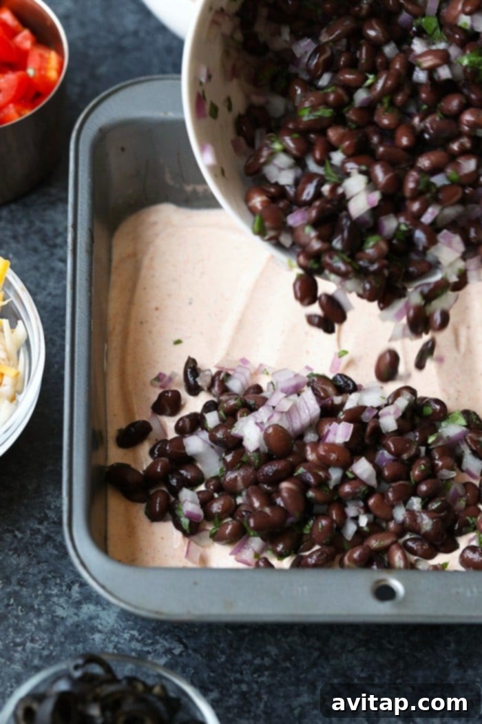 Black bean and cilantro mixture being spread as the third layer in a Healthy 7 Layer Greek Yogurt Taco Dip