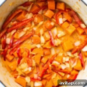 A pot filled with sweet potatoes, carrots, onions, garlic, and red peppers, sautéing to perfection.