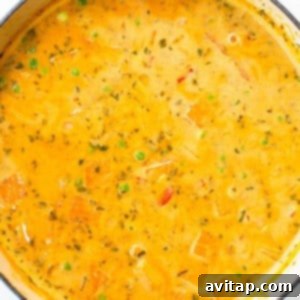 A close-up of the fragrant coconut curry soup, gently simmering with green peas and colorful vegetables in a blue pot.