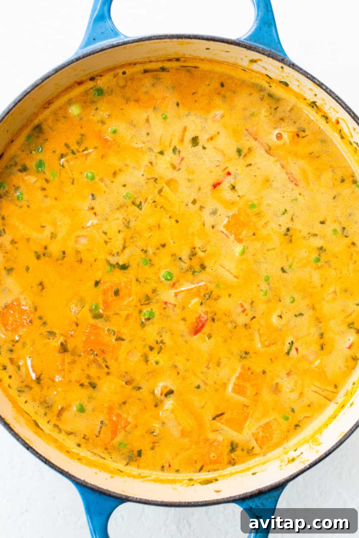 A close-up shot of the creamy coconut curry soup in a rustic blue pot, showcasing the vibrant broth and tender vegetables, simmering gently.