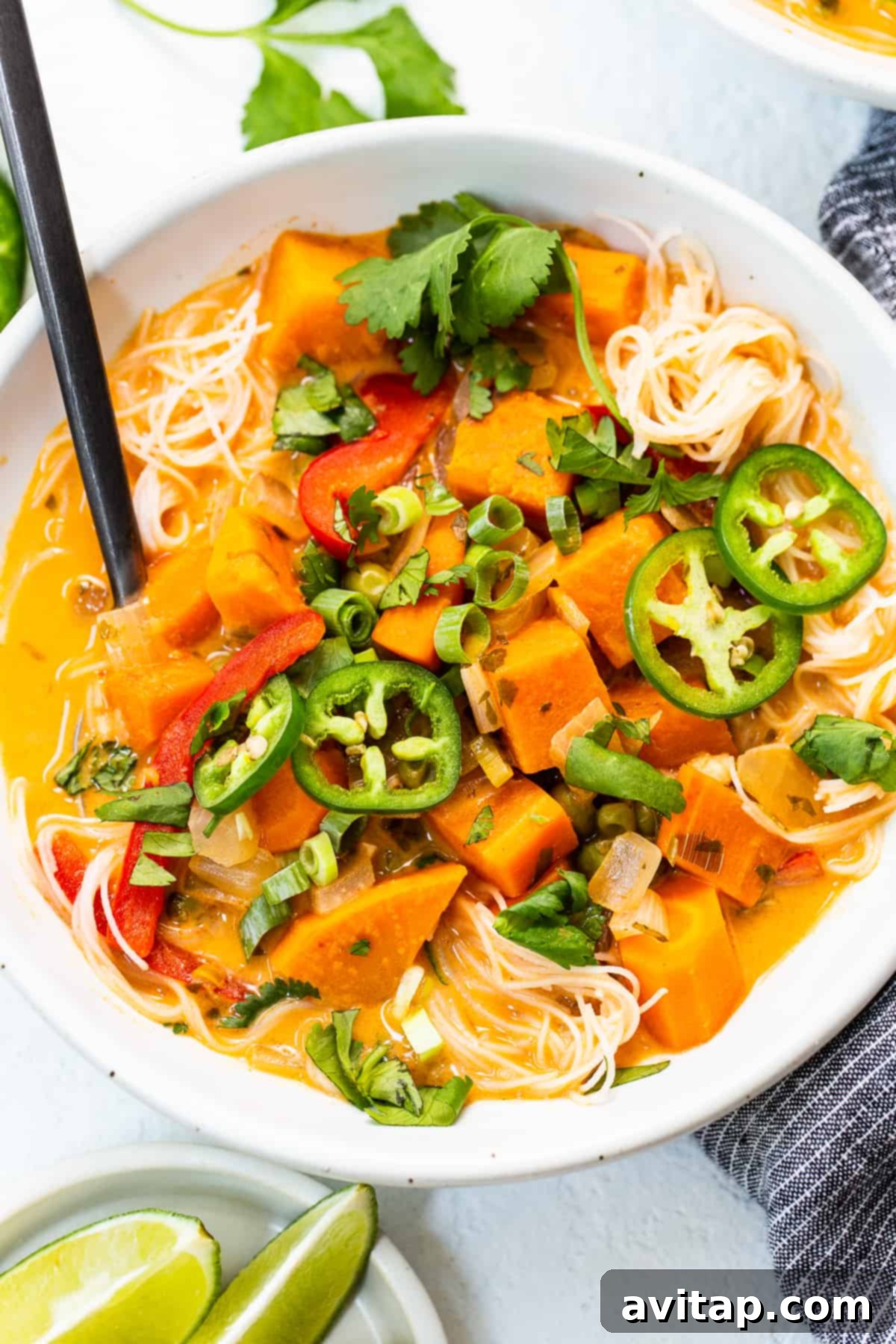 A vibrant bowl of coconut curry soup, generously topped with fresh cilantro, sliced green onions, and fiery red jalapeños, making for an inviting meal.