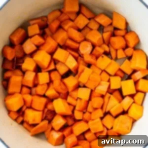 Cubed sweet potatoes and carrots beginning to soften in a blue pot with coconut oil.
