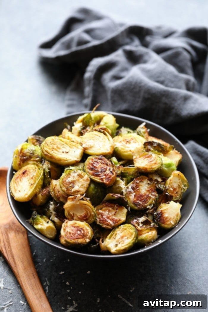 These roasted Brussel sprouts with parmesan are a great side dish staple for any time of year! All you need are 6 ingredients in order to make these crunchy, cheesy bites of heaven. Close-up of golden brown roasted Brussels sprouts with melted parmesan cheese, garnished with fresh herbs in a serving bowl.