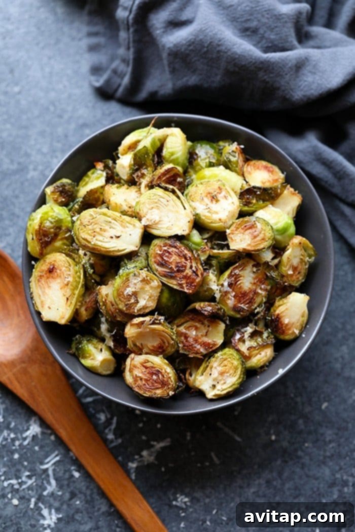 These roasted Brussel sprouts with parmesan are a great side dish staple for any time of year! All you need are 6 ingredients in order to make these crunchy, cheesy bites of heaven. A bowl of freshly roasted Brussels sprouts with melted parmesan cheese and a sprig of rosemary.