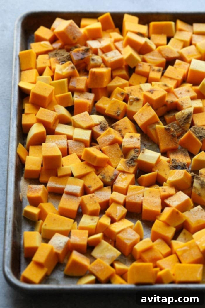Cubed butternut squash seasoned with olive oil and spices, spread on a baking sheet, ready for the oven.