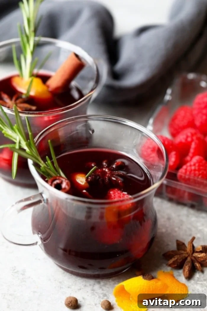 A beautiful glass mug brimming with ruby-red spiced raspberry mulled wine, garnished with a cinnamon stick, star anise, and fresh raspberries, sitting elegantly on a rustic wooden table.