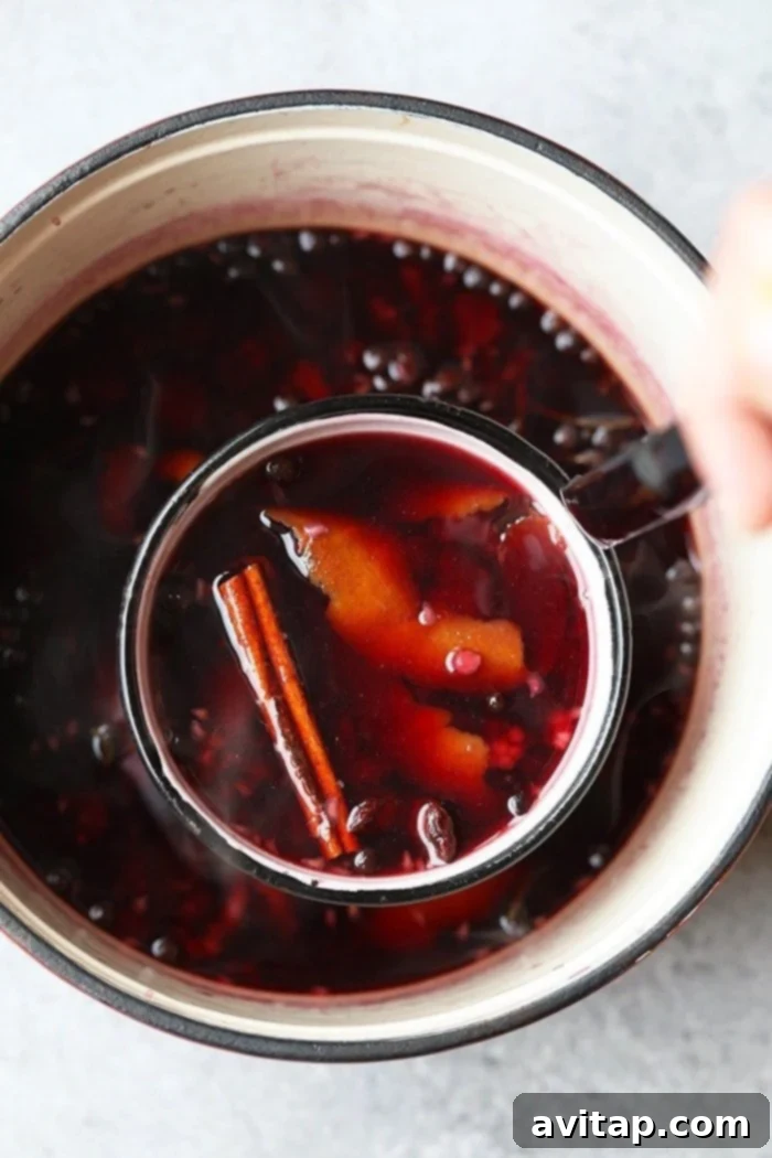 A large stock pot filled with red wine, fresh raspberries, orange slices, and whole spices simmering gently on a stovetop, creating an aromatic cloud of steam.