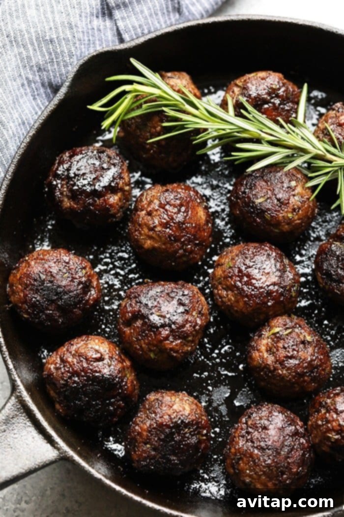 Perfectly cooked Rosemary Thyme Balsamic Meatballs garnished with fresh herbs in a cast iron pan, ready to be served.