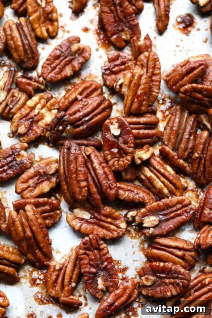 Freshly roasted maple pecans spread in a single layer on a parchment-lined baking sheet, glistening with caramelized syrup.