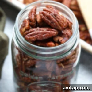 Roasted pecans displayed in a glass jar with a wooden spoon.