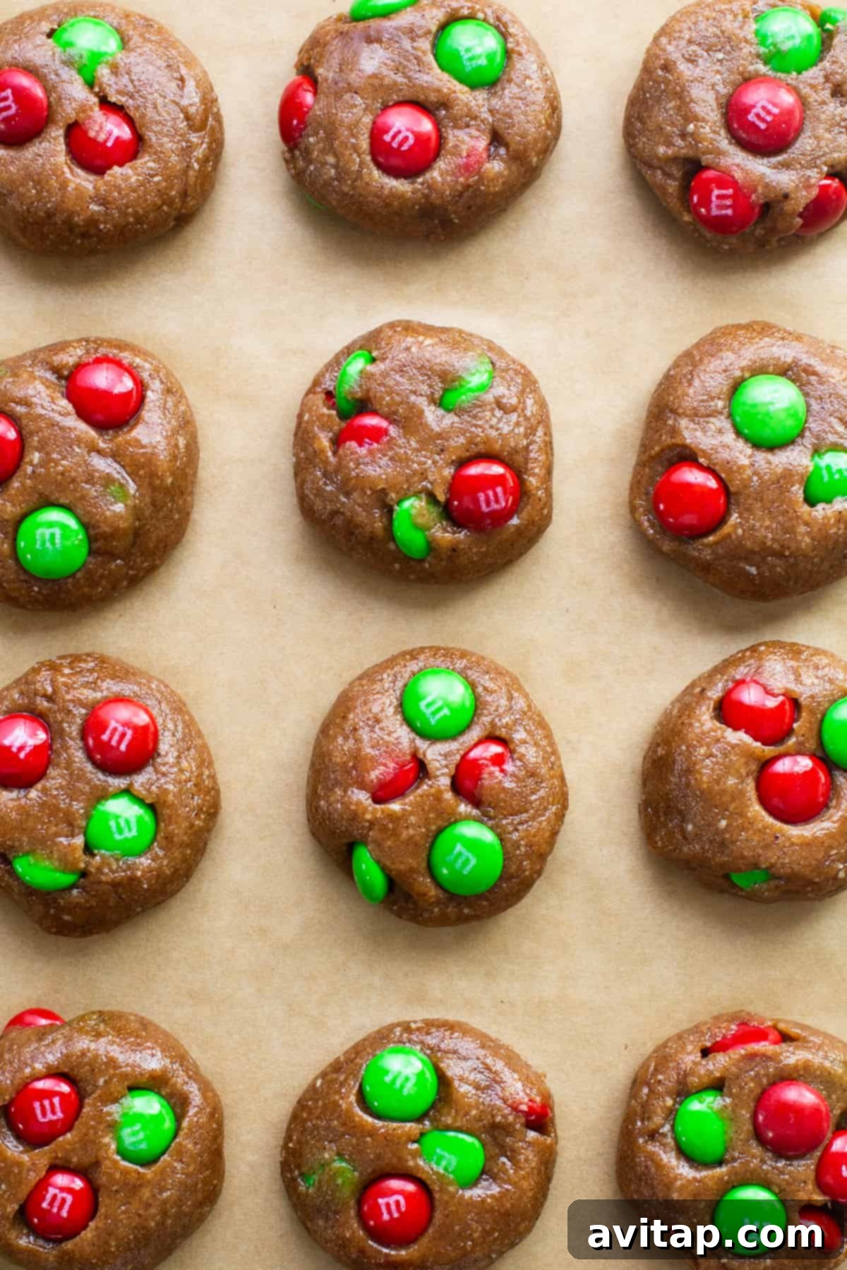 Flourless M&M cookies baking on a sheet, with vibrant green and red M&Ms visible on a parchment-lined tray.