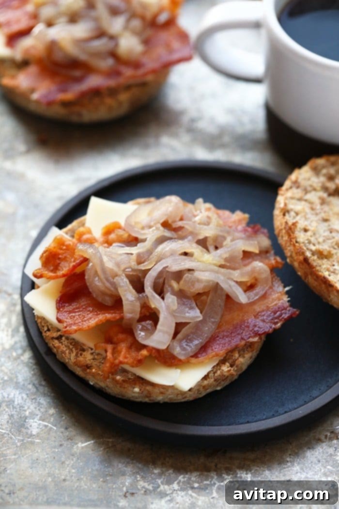 Close-up of a disassembled Arugula Breakfast Sandwich with Caramelized Onions, showcasing the fluffy egg, crispy bacon, and golden onions on a toasted English muffin.