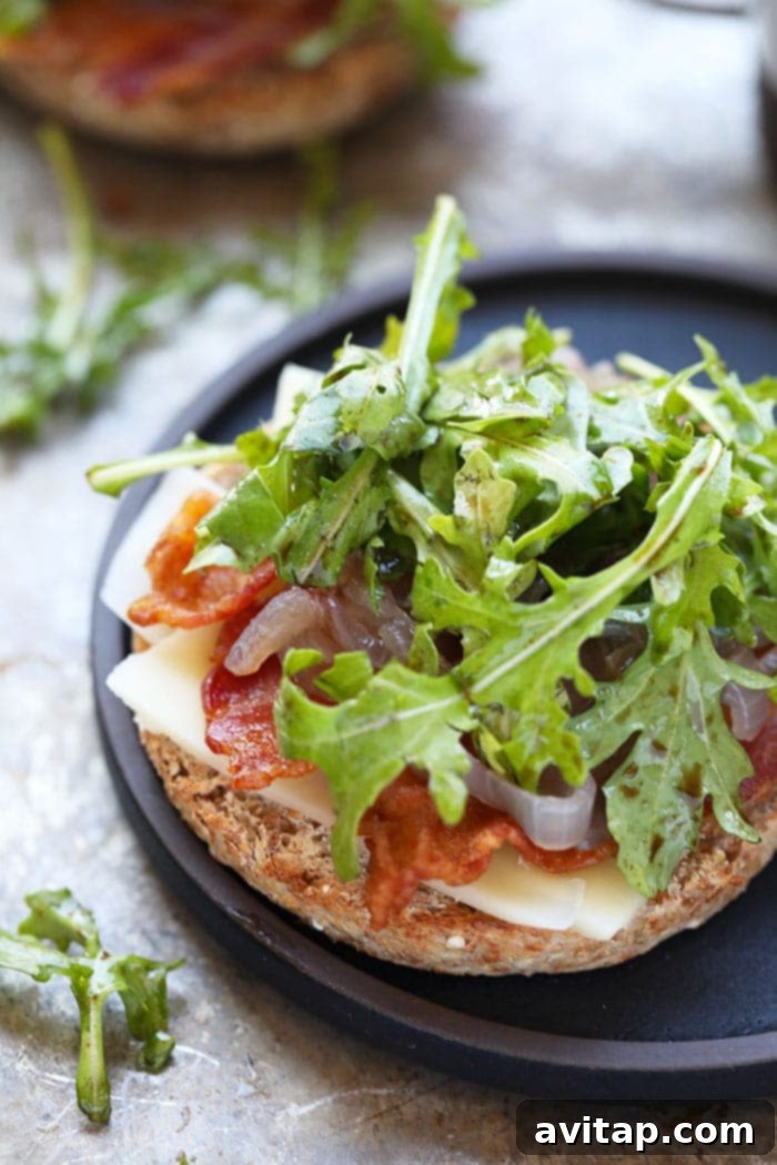 A stack of three gourmet Arugula Breakfast Sandwiches with Caramelized Onions, each featuring a golden fried egg, crispy bacon, and vibrant arugula on a toasted whole-grain English muffin.
