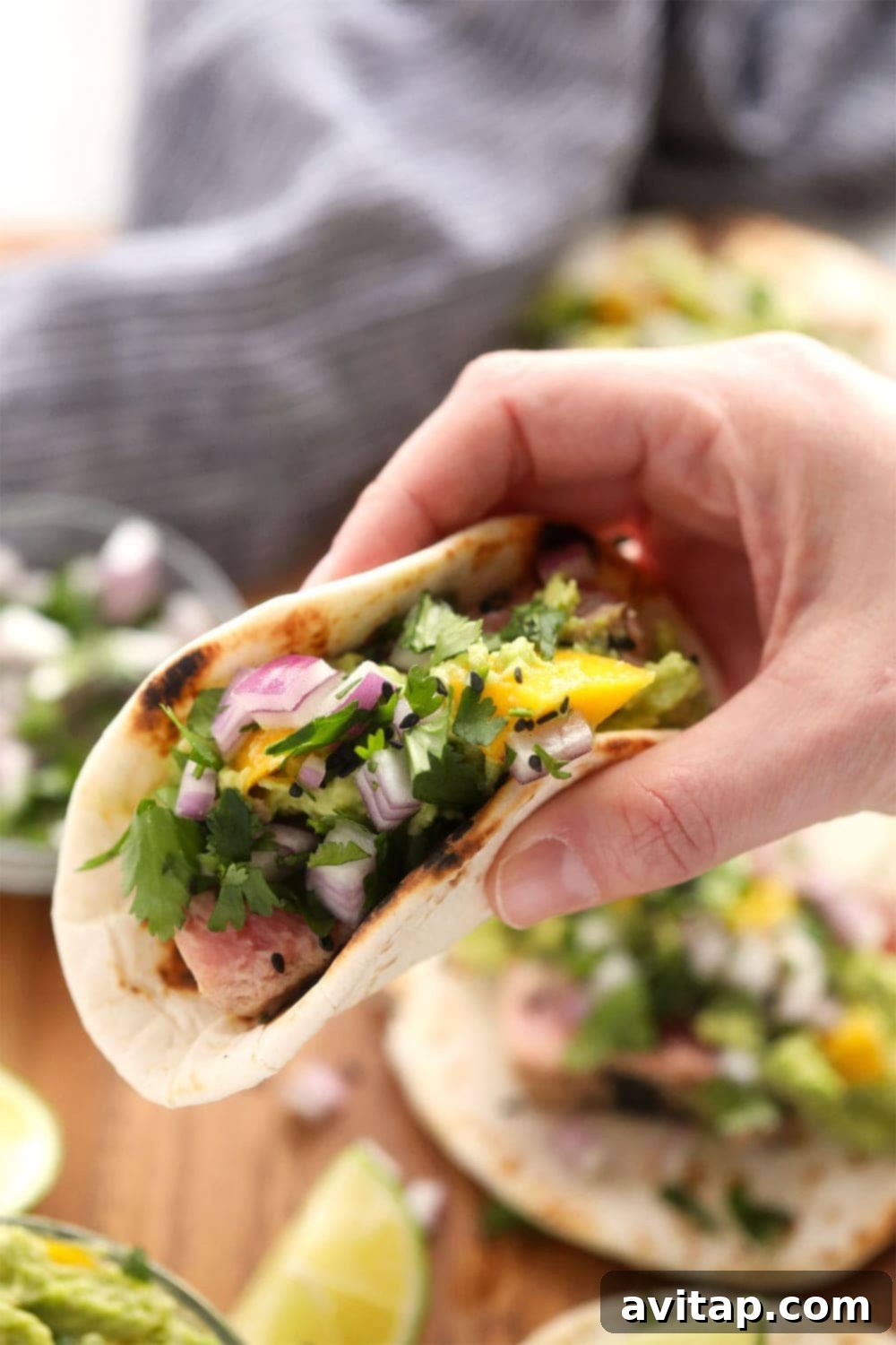 Gorgeous Ahi Tuna Tacos that are perfectly seared with sesame seeds and served with a citrus mango guacamole! holding an ahi tuna taco