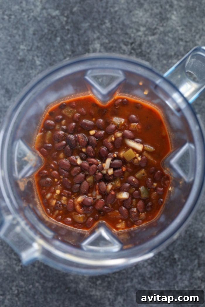 Blending Black Bean Soup with Immersion Blender An immersion blender being used to puree a portion of the black bean soup directly in the slow cooker, creating a creamy texture.
