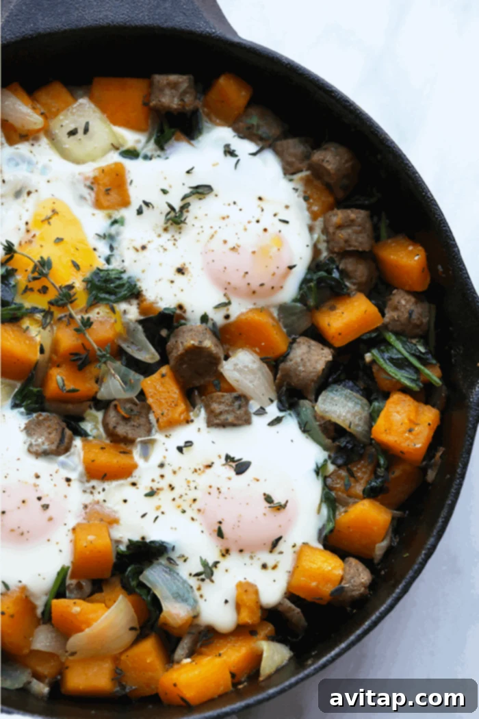 A hearty butternut squash breakfast hash with sausage and baked eggs in a cast iron skillet, ready to eat.