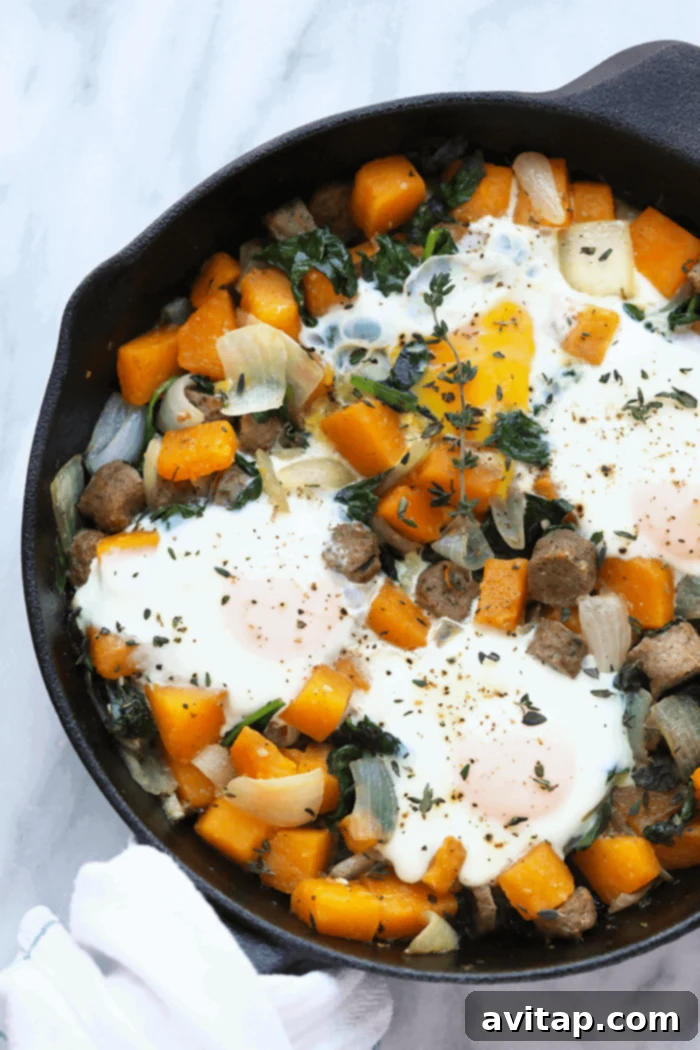 Close-up of butternut squash breakfast hash cooking in a cast iron skillet with eggs baked into divots.
