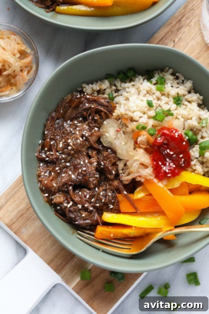 A vibrant Instant Pot Korean Beef Bowl with tender shredded beef, colorful bell peppers, and fluffy rice, garnished with sesame seeds and green onions.