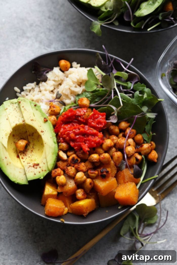 A beautifully arranged Butternut Squash Buddha Bowl, showcasing vibrant ingredients like roasted squash, green leaves, chickpeas, and avocado.