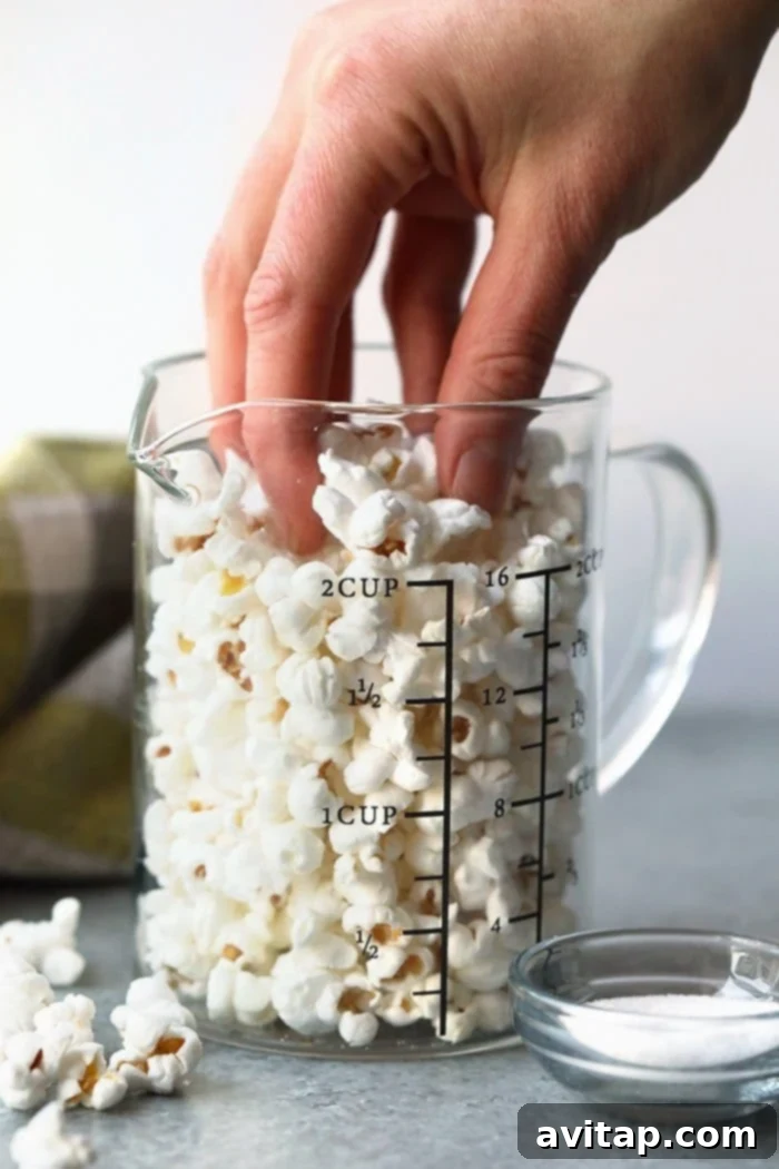 Hand reaching for perfectly popped popcorn in a clear glass bowl, showcasing a healthy and easy stovetop snack