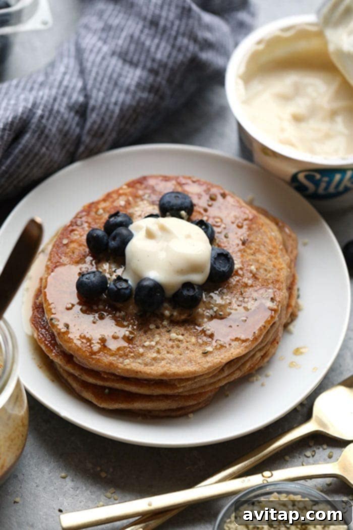 Stack of fluffy vegan banana pancakes on a white plate with fresh berries and maple syrup.