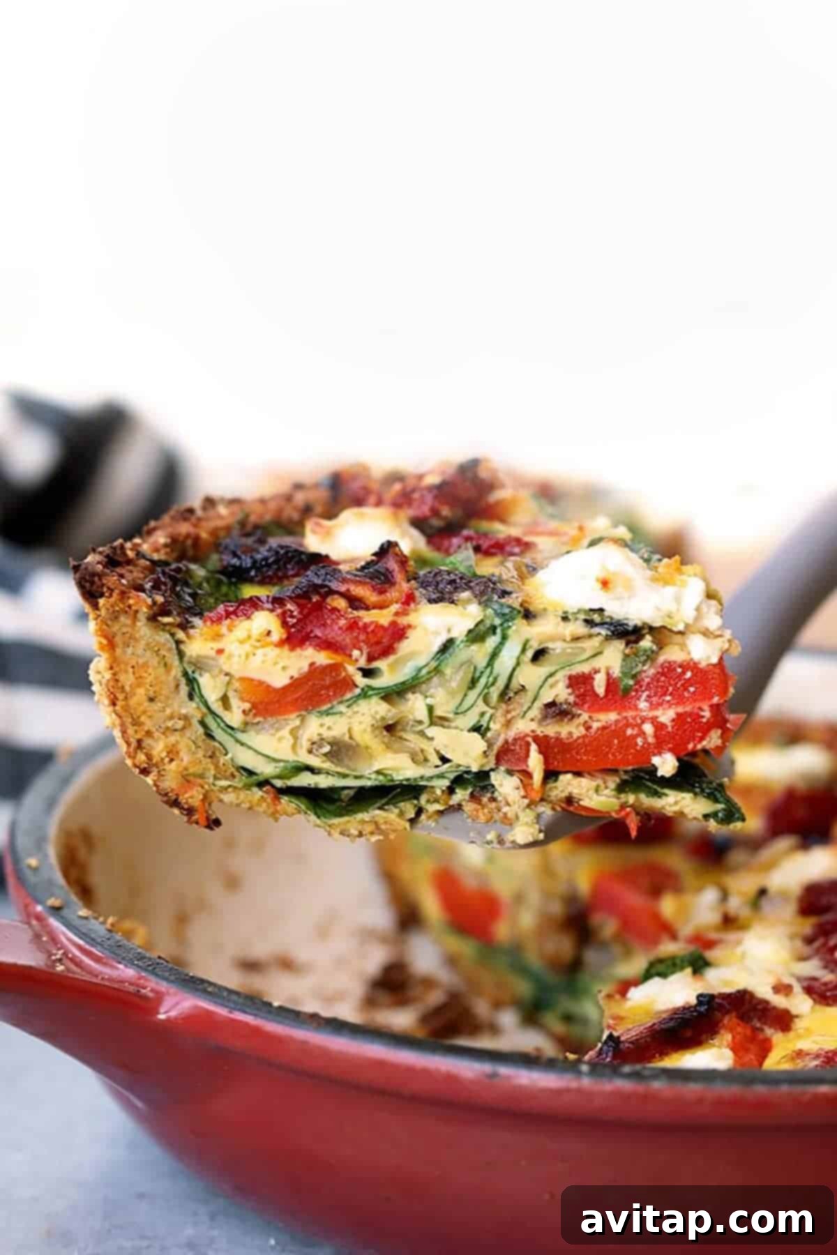 A perfect wedge of sweet potato crust quiche, highlighting the layered filling of eggs, vegetables, and goat cheese, served on a white plate.
