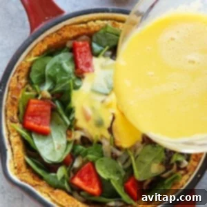 Pouring egg mixture into a skillet with spinach, red bell peppers, and sweet potato crust for quiche preparation.