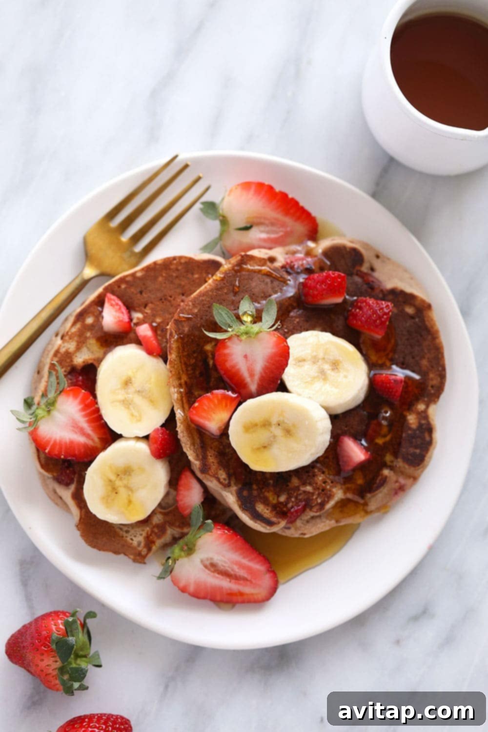 Delicious Whole Grain Strawberry Blender Pancakes A beautifully stacked plate of fluffy strawberry pancakes, generously topped with fresh strawberries and a drizzle of golden maple syrup, ready to be enjoyed.