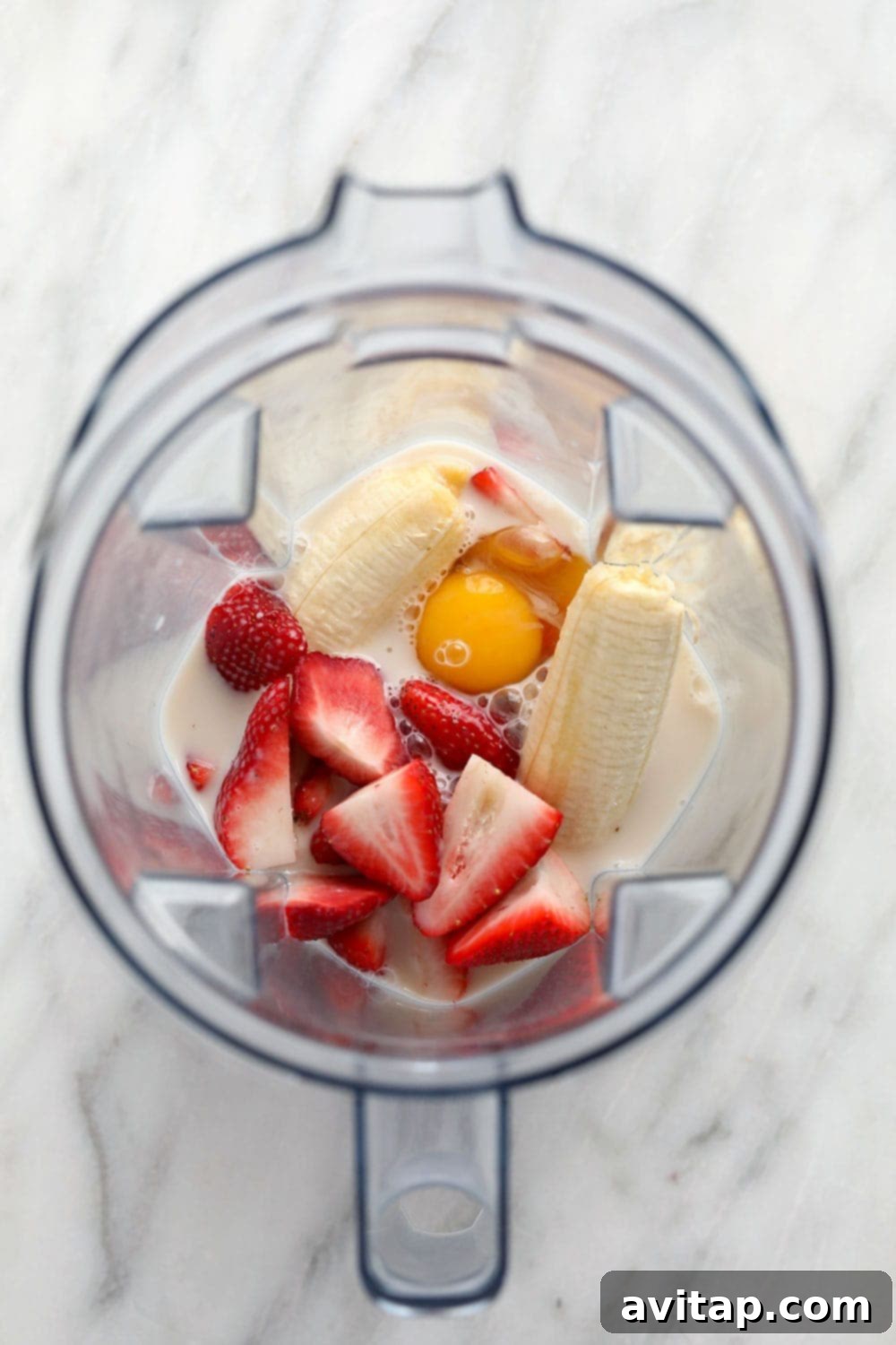 Essential Ingredients for Blender Pancakes Close-up of fresh ingredients for healthy strawberry pancakes, including banana, whole strawberries, white whole wheat flour, eggs, almond milk, and honey, all ready to be blended.