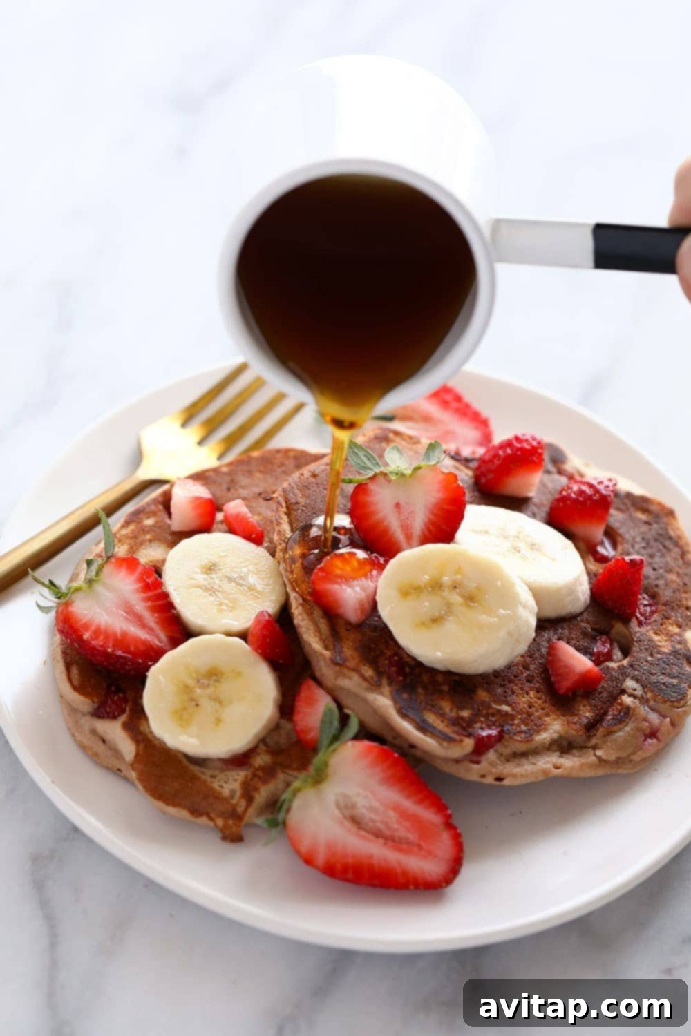 Plated Healthy Strawberry Pancakes A stack of golden-brown strawberry pancakes on a clean white plate, artfully garnished with fresh whole strawberries and drizzled with a rich amber syrup.